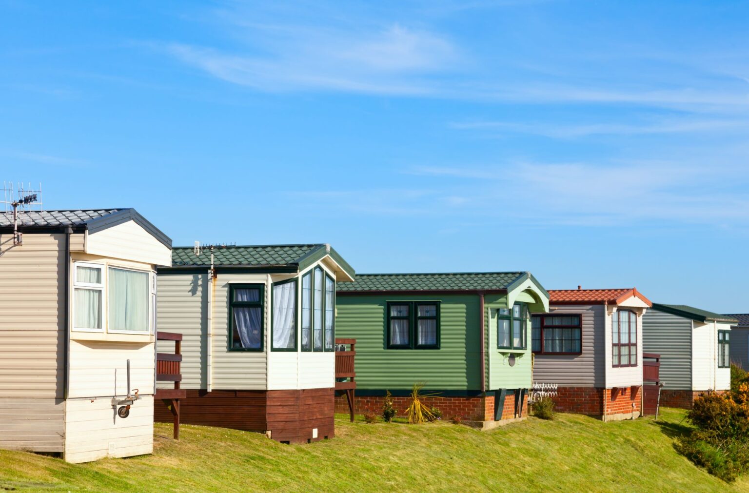 A row of mobile or manufactured homes in shades of white, green, and pink, as one might see during a manufactured home inspection or a prefab home inspection.