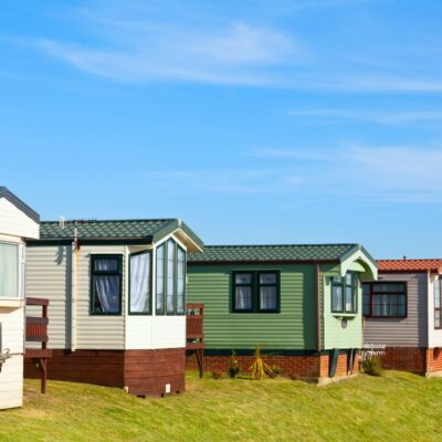 A row of mobile or manufactured homes in shades of white, green, and pink, as one might see during a manufactured home inspection or a prefab home inspection.