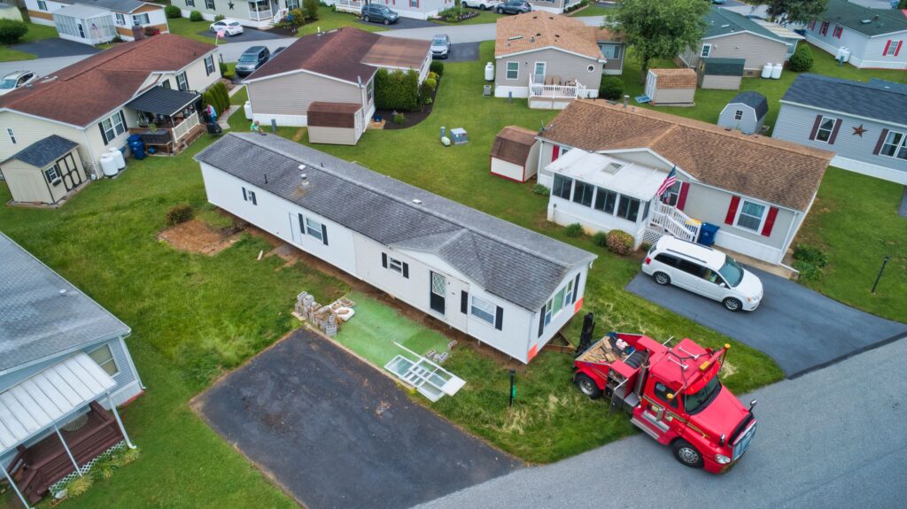 An aerial view of a truck delivering a manufactured home to its new location, surrounded by other manufactured homes.