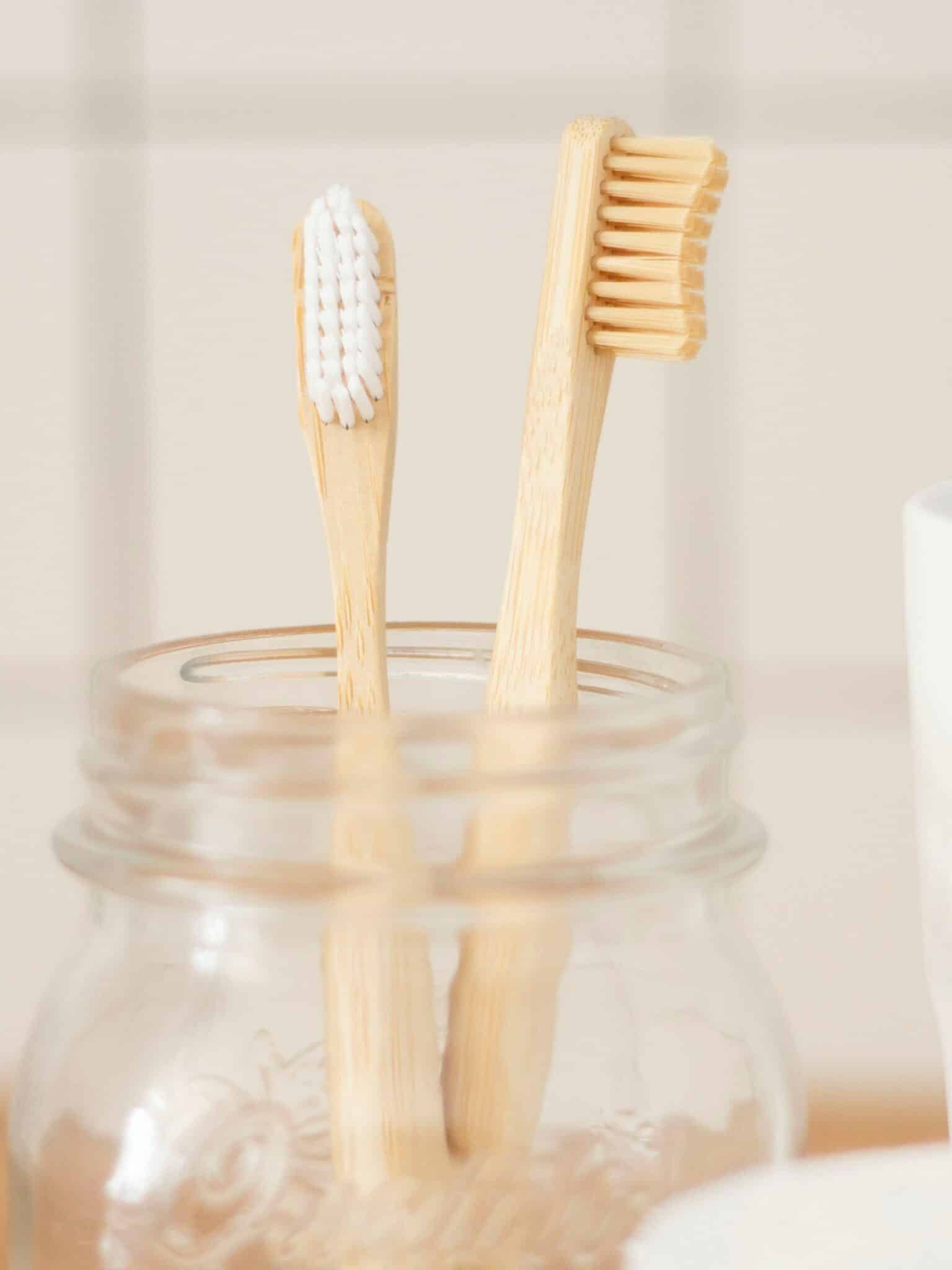 Two light-brown toothbrushes in a glass canning jar against an off-white wall