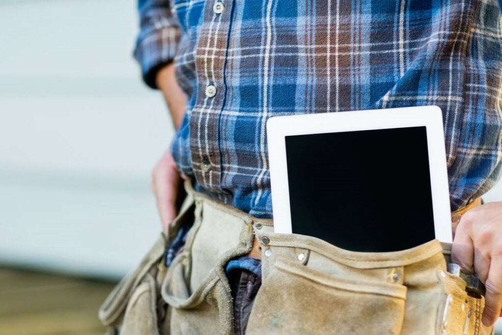 Close up of man’s waist with leather home inspector tool belt over cargo pants and flannel shirt. Belt carries home inspection equipment and tools like a digital tablet.