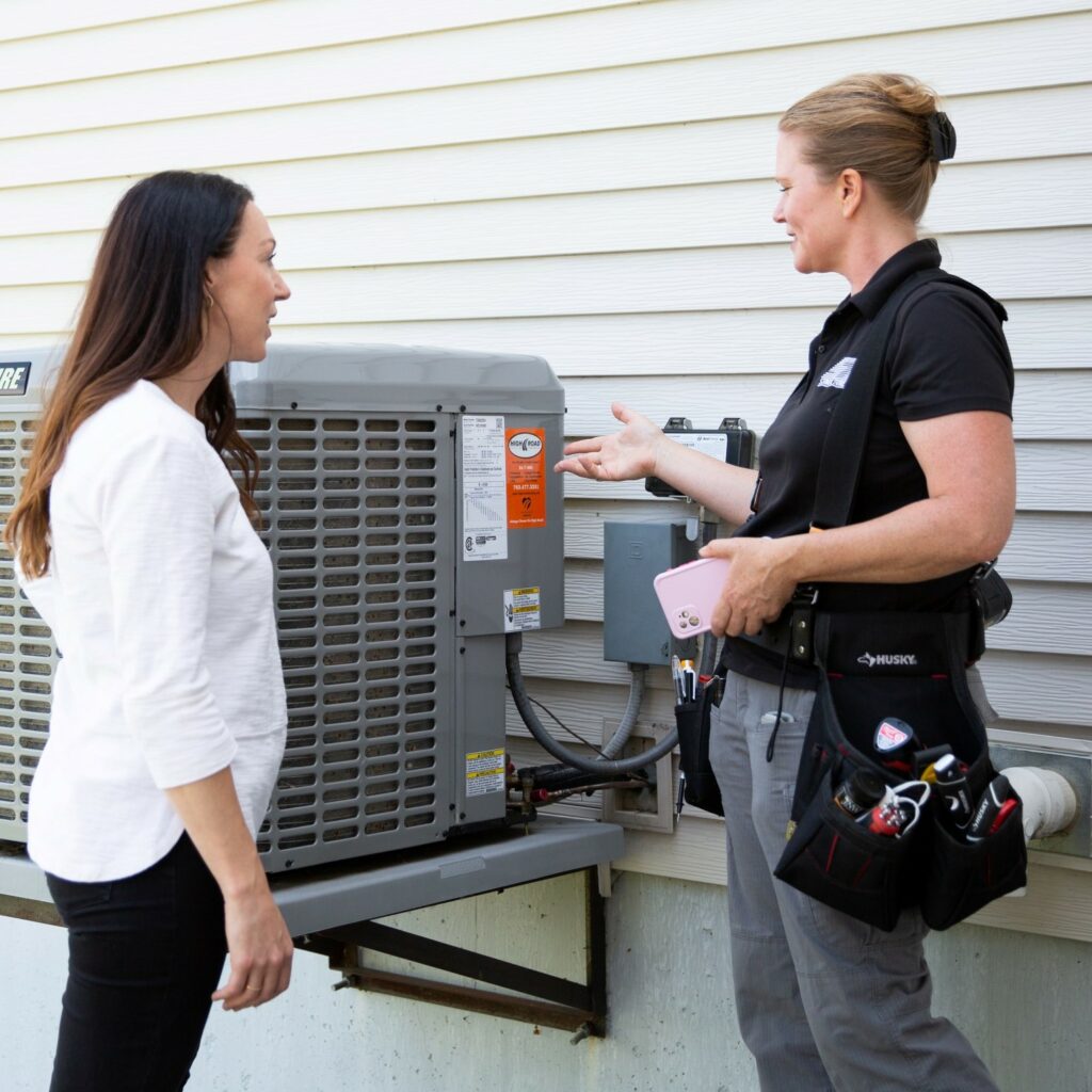 Structure Tech Home Inspector alleviates home inspection seller anxiety by educating her on HVAC system onsite. Two women chat by HVAC unit.