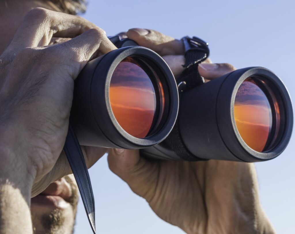 Male home inspector holds up binoculars and looks through them, as if viewing the roof in this roof leak home inspection claim.