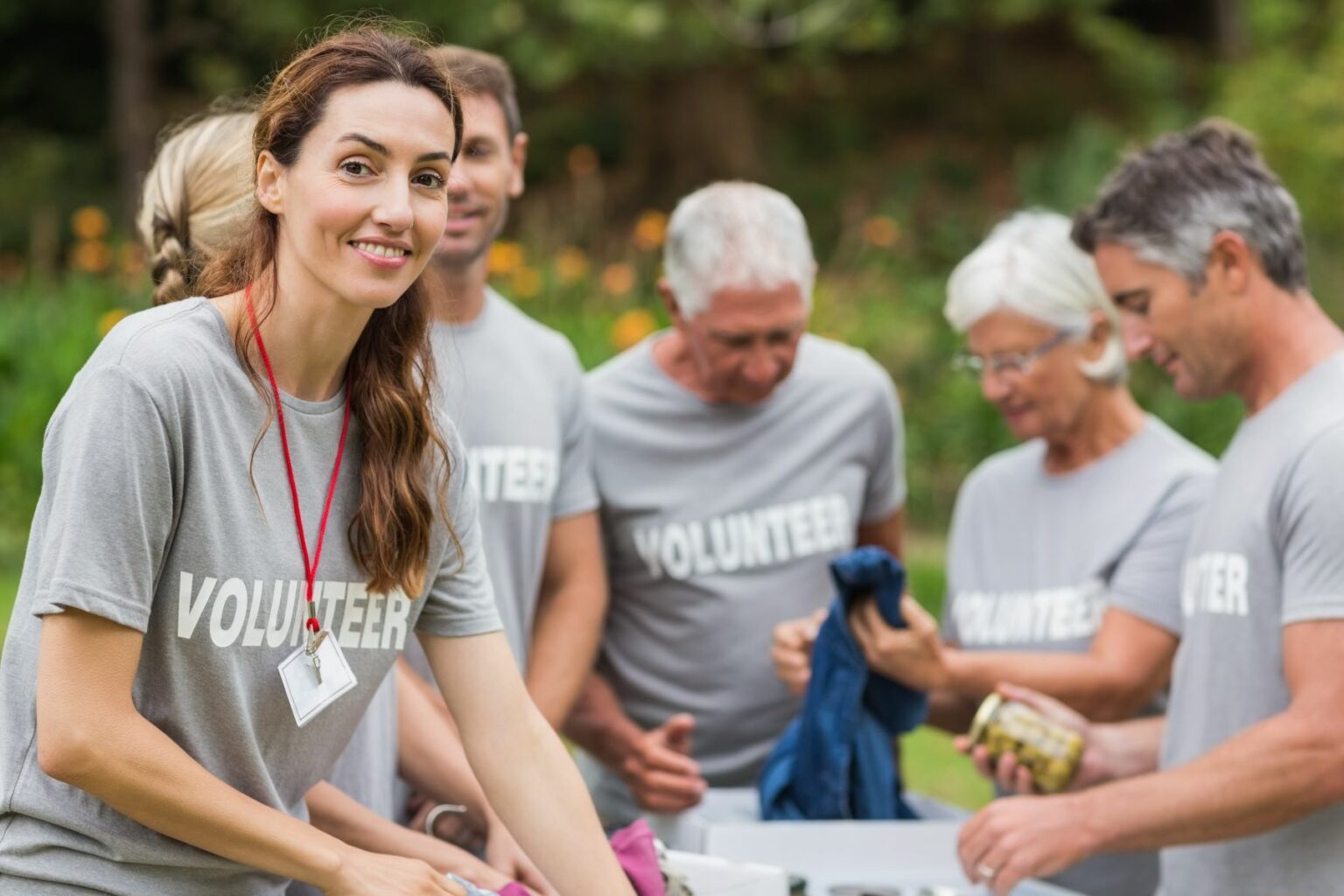 Group of people wearing grey “volunteer” t-shirts and sorting through boxes of clothes. One volunteer smiles at the camera. Engaging with your local community as a home inspector, perhaps through community service volunteering, boosts local home inspectors’ connections.