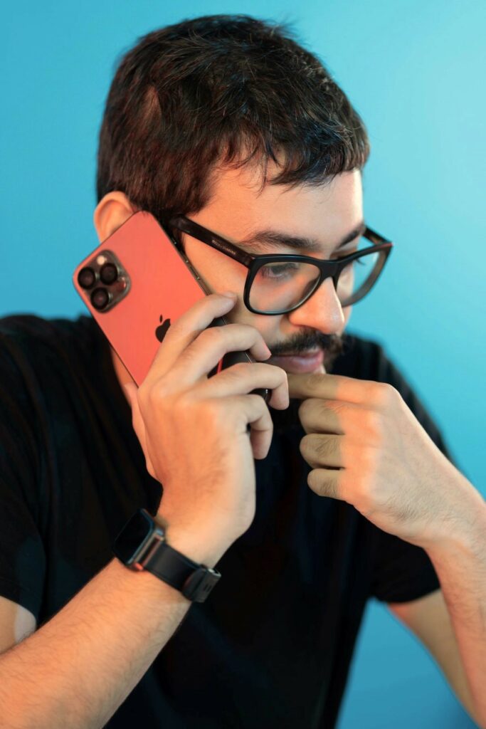 Man wearing glasses, black shirt, and black watch holds a smart phone to his ear and appears deep in thought, as if discussing a rental property inspection.