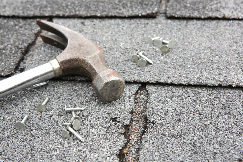 Roof repair costs shown with zoomed-in roof shingles, a hammer, and nails, highlighting a case where a home inspector missed a leaking roof.