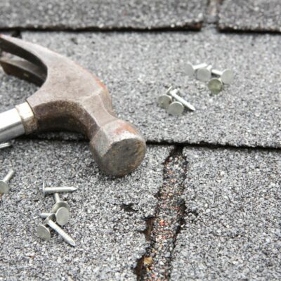 Roof repair costs shown with zoomed-in roof shingles, a hammer, and nails, highlighting a case where a home inspector missed a leaking roof.