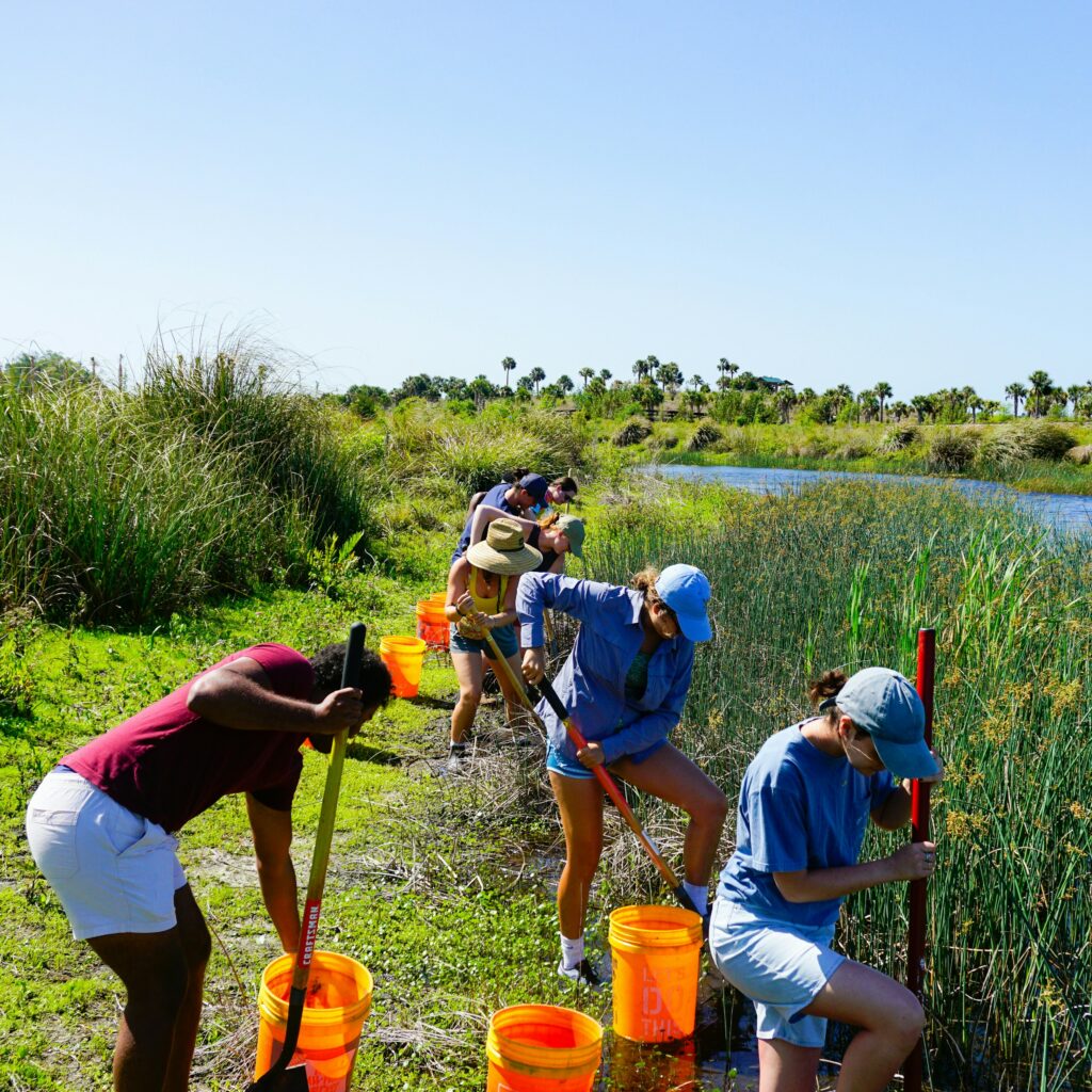 A group of people volunteering to pick up trash along a river. Community service is excellent for engaging with a local community as a home inspector.