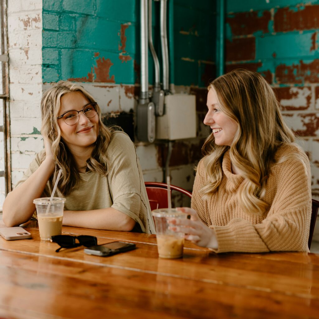 Two women sitting together at a coffee shop table, each with a plastic cup of coffee. Creating a home inspector's community means networking and building these friendships with other inspectors.