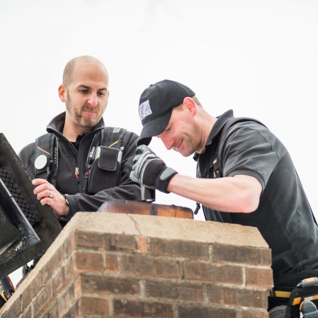 Experienced inspector offers home inspector job training to another inspector. Both are standing on a roof looking down at a chimney. Photo courtesy of Structure Tech Home Inspections.