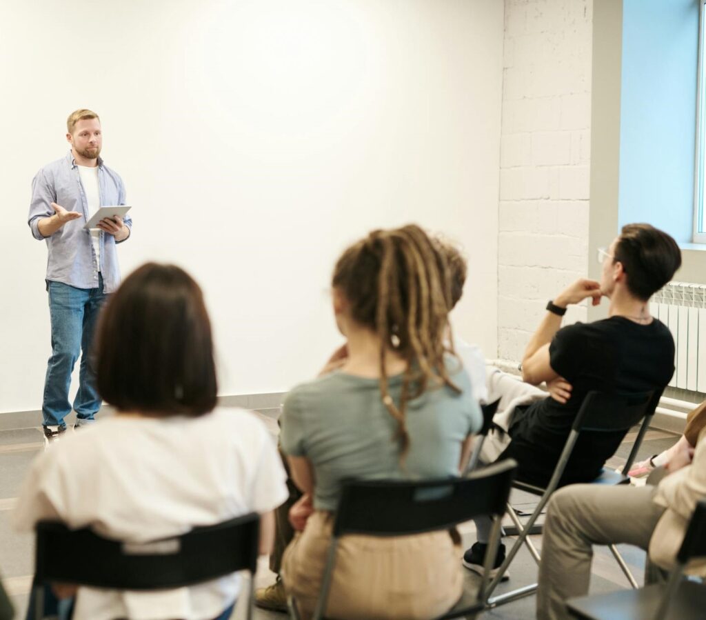 A man stands at the front of a classroom mentoring and teaching other home inspectors in the audience.