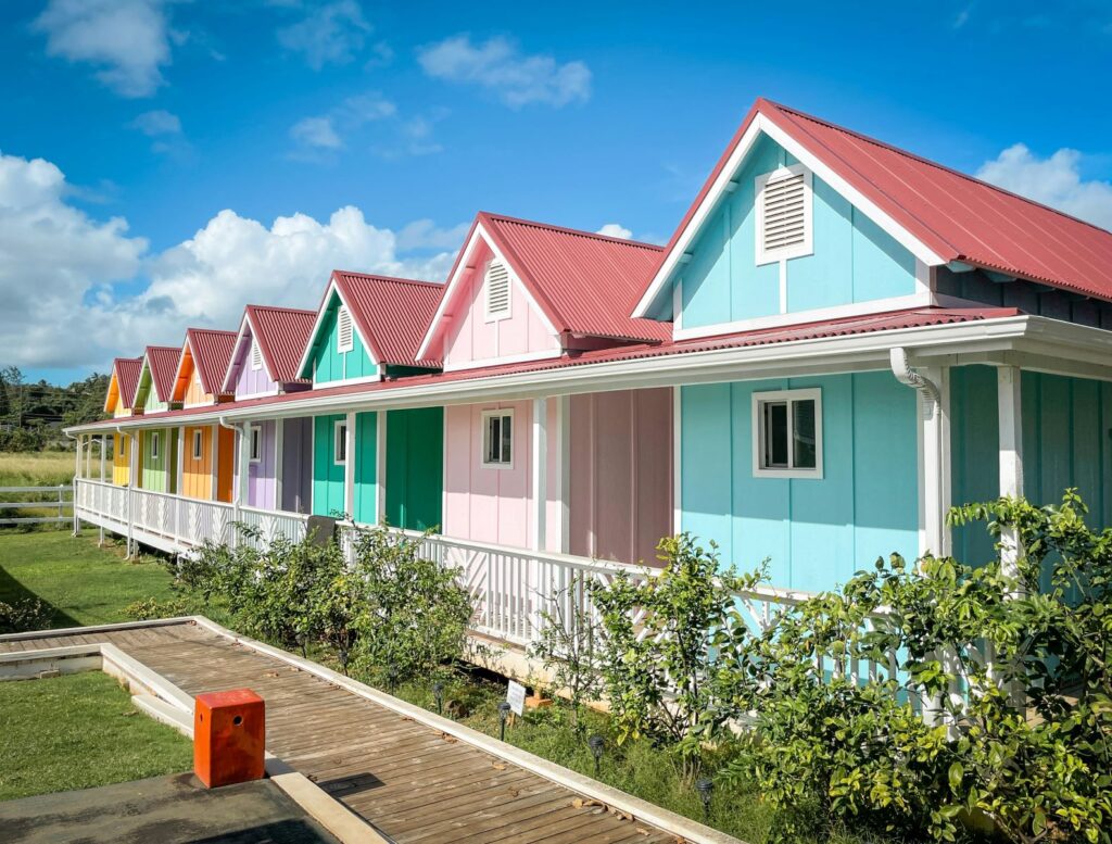 Seven pastel-colored tiny houses surrounded by green grass and a bright, blue sky in Hawaii.