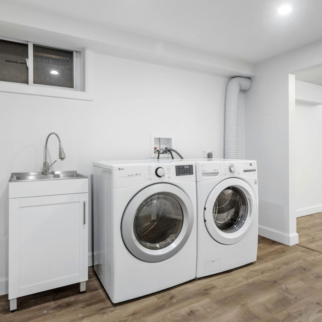 A standalone sink and faucet, washing machine, and dryer lined up in a basement laundry room, where water intrusion detection is especially important.