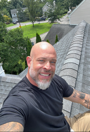 Joe Mazza of Exclusive Home Inspections sits on a roof smiling at the camera, as if explaining how water intrusion in a home  happens through the roof.