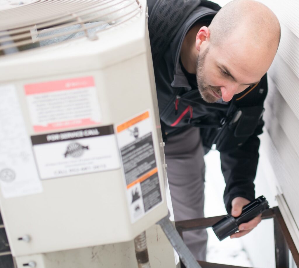 Home inspector evaluates HVAC unit with flashlight.