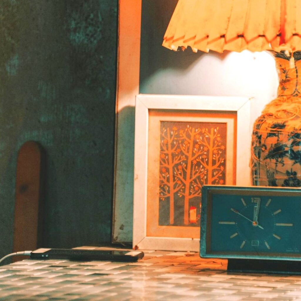 Vintage lamp and alarm clock displaying old electrical wiring next to a charging smartphone, which would require major electrical upgrades to accommodate today’s energy consumption.