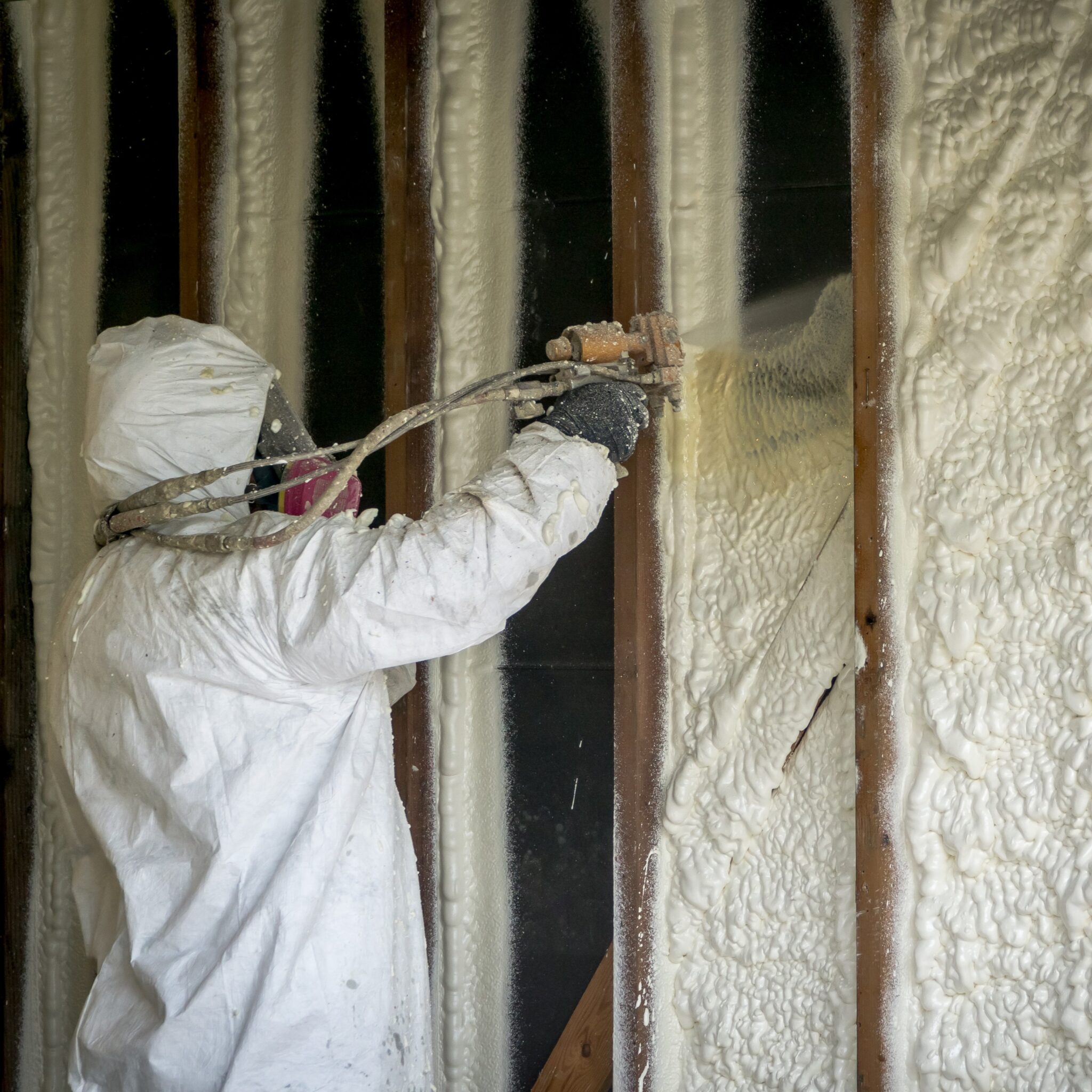 Worker wearing PPE installs closed-cell foam spray in an attic.