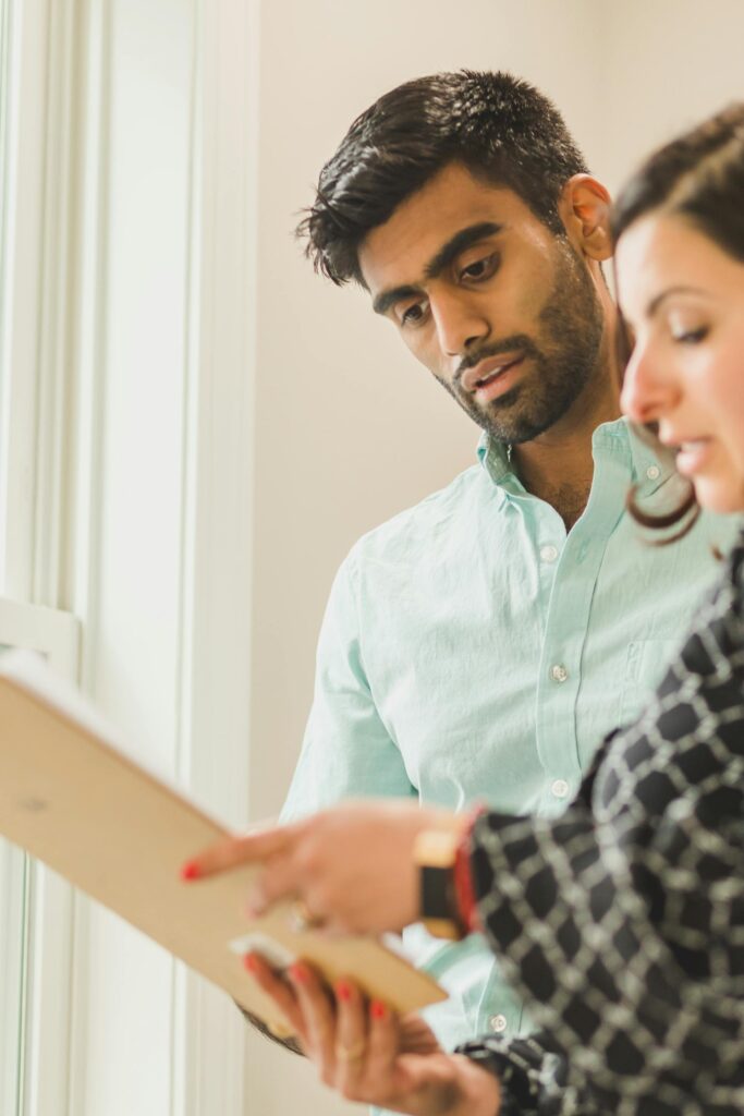 Real estate agent tells client about home inspections, showing him a clipboard with paperwork like inspection pricing.